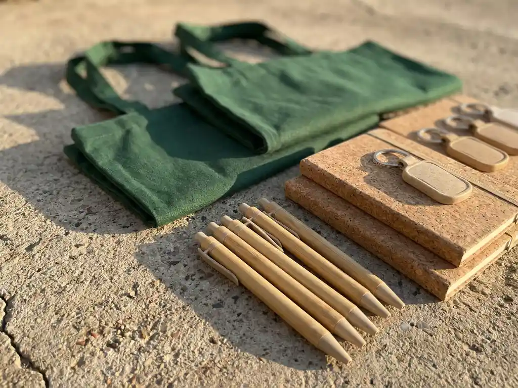 Duurzame relatiegeschenken op beton: bamboe pennen, gerecyclede katoenen tassen, kurken notitieboekjes en tarwestro sleutelhangers.